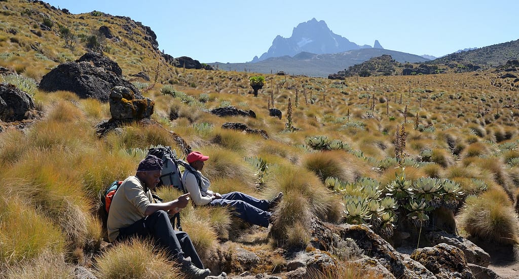 Keshi Tours porters and guides resting on moorland with Mount Kenya peak view - Mount Kenya Climbing Guide